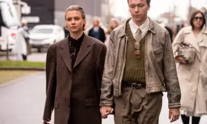 Ein Paar im **Copenhagen Style** geht Händchen haltend. Sie trägt einen braunen Oversize-Blazer, er eine Lederjacke über einem Strickpullover.