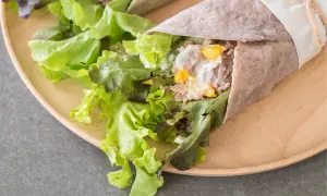 Świeża tortilla z tuńczykiem, chrupiącą sałatą i kukurydzą, zawinięta w papier i przewiązana sznurkiem.