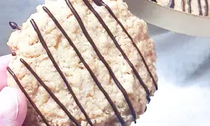 En hand håller en gammaldags havrekaka med chokladdrizzle. Kakans textur är grov och inbjudande.