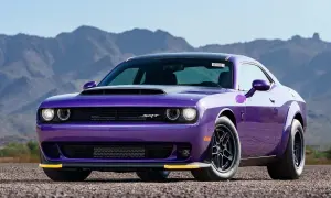 En lila amerikansk sportbil, en Dodge Challenger SRT, står parkerad på en grusväg med berg i bakgrunden.