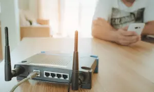 Router z antenkami tworzy domowy hotspot. W tle osoba korzysta z telefonu.