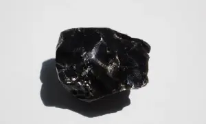Błyszczący, czarny obsydian, kamień o niezwykłych właściwościach, leży na białym tle.