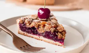 Une part de tarte aux cerises généreuse, garnie d'une cerise fraîche et saupoudrée de sucre glace et d'amandes effilées.