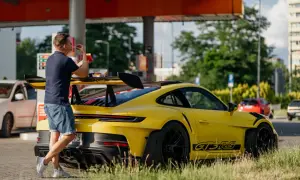 Żółty Porsche 911 GT3 RS z wielkim skrzydłem, obok którego stoi mężczyzna jedzący frytki.