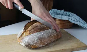 Ręka kroi złocisty bochenek chleba na desce.