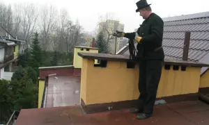 Kominiarz w cylindrze przygotowuje się do przeglądu kominiarskiego, trzymając w rękach liny.