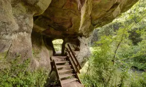 Holztreppe führt aus einer Felsgrotte auf dem schwarzachklamm wanderweg. Ein Fluss plätschert im Hintergrund.
