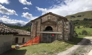 Il rifugio Città di Amandola, con la sua facciata in pietra e legno, è circondato da un paesaggio verdeggiante sotto un cielo azzurro con nuvole bianche.