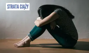 Smutna kobieta siedzi skulona na podłodze, przeżywając stratę ciąży.