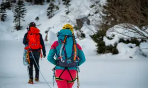 Dwóch alpinistów w zimowych strojach, z plecakami i sprzętem, przemierza ośnieżony teren. To inspiracja, co zabrać w góry zimą.