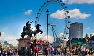 Fakta om London Eye: ett pariserhjul med gondoler, en staty av en häst och vagn, och en folkmassa på en solig dag.