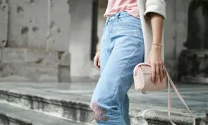 Frau in Jeans mit Blumenstickerei und rosa Tasche. Ein Symbol für die Probleme von Fast Fashion, die oft auf Kosten von Mensch und Umwelt gehen.