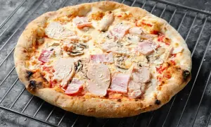 Eine knusprige Pizza mit Schinken und Pilzen auf einem Gitterrost.