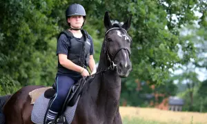 Młoda amazonka w kasku i kamizelce ochronnej siedzi na ciemnym koniu. Stajnia Profit Orzesze to jej bezpieczne miejsce.