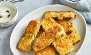 Knuspriges Zucchini-Schnitzel auf einem Teller, daneben eine Schale mit Dip und Gabeln.