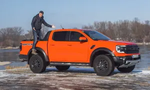 Pomarańczowy Ford Ranger Raptor z mężczyzną stojącym na pace, gotowy na przygodę.