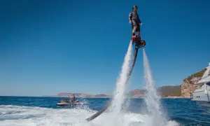 Mężczyzna na flyboardzie i osoba na skuterze wodnym na tle morza i klifów.