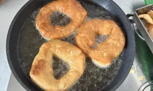 Tre ciambelle fritte dorate sfrigolano nell'olio caldo, pronte per essere gustate.