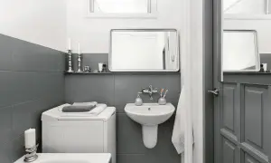 Baño moderno con azulejos grises, lavadora y lavabo. Un ejemplo de reformas de baños antes y después, con un estilo minimalista y funcional.