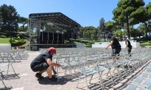 Preparando el escenario para conciertos en el Jardín de Invierno de Zaragoza. Hombres colocan sillas metálicas en filas.