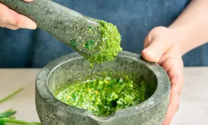 Frische Kräuter werden im Mörser zerstoßen, um ein leuchtend grünes Pesto zuzubereiten. Perfekt für einfache Pesto Rezepte.