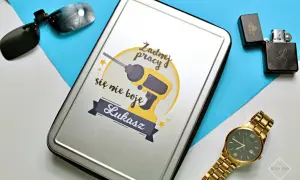 Prezent na dzień chłopaka dla Łukasza: metalowe pudełko z wiertarką i napisem "Żadnej pracy się nie boję", obok okulary, zapalniczka i złoty zegarek.