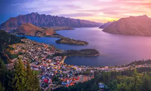 Vacker solnedgång över Queenstown, Nya Zeeland. Staden ligger vid en sjö, omgiven av berg och skog.