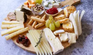 Una deliciosa presentación tabla de quesos con variedad de quesos, uvas, frutos secos y panecillos.