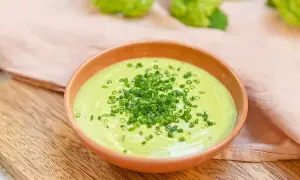 Grön, krämig salsa verde toppad med finhackad gräslök i en skål på en träskärbräda.