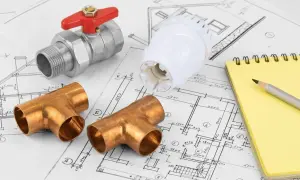 Planowanie instalacji grzewczej do domu 100m2: zawór, trójniki miedziane, głowica termostatyczna i notatnik.