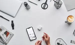 Dłonie trzymające białe słuchawki AirPods obok smartfona i etui.