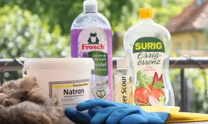 Wollprogramm Waschmaschine: Natron, Essigessenz und Reinigungsmittel für die schonende Wäsche. Blaue Handschuhe liegen bereit.