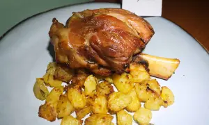 Stinco di maiale succulento e dorato, servito con patate arrosto croccanti e profumate al rosmarino.