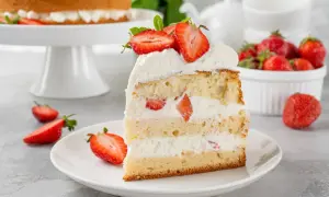Puszysty biszkopt przełożony kremem z mascarpone i kawałkami truskawek, udekorowany świeżymi owocami.