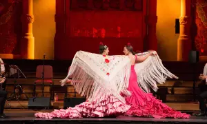 Dos bailarinas de flamenco, con vestidos rosas y mantones bordados, despliegan su arte. El escenario tiene un aire de tener aje.