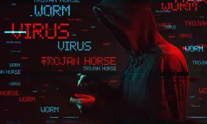 Haker w kapturze, otoczony przez migoczące napisy "WORM", "VIRUS" i "TROJAN HORSE". To pokazuje, co to trojan - złośliwe oprogramowanie udające coś pożytecznego.