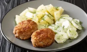Dwa kotlety mielone z ziemniakami i mizerią na talerzu.