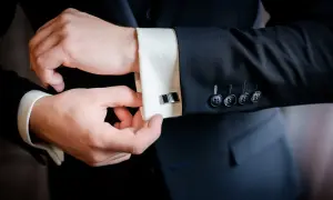 Mężczyzna zapina eleganckie spinki do mankietów koszuli, pokazując jak zapiąć spinki do koszuli.