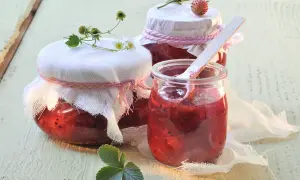 Gläser mit selbstgemachtem Erdbeerkompott, bereit zum Einkochen. Ein Holzlöffel steckt in einem Glas.
