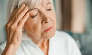 Starsza kobieta z ręką na skroni, zamyślona. Może to być jeden z objawów choroby Alzheimera.