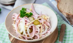 Ein köstlicher schweizer Wurstsalat mit Gurken, Zwiebeln und Käse, garniert mit Petersilie.