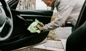 Man rengör bilens dörrpanel med en grön trasa. En fräsch doft i bilens interiör är målet.