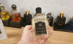 Kolekcja perfum Creed, w tym Creed Royal Oud, prezentowana na drewnianym blacie. W dłoni trzymana jest butelka Creed Royal Oud.