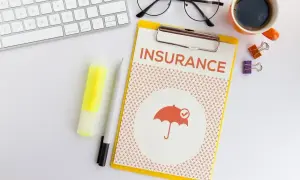 Planujesz ubezpieczenie zdrowotne bez pracy? Na biurku dokument "INSURANCE" z parasolką, klawiatura, okulary i kawa.