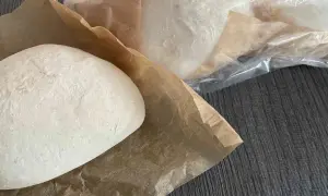 Frische Pizzaböden, bereit für das Pizzateig einfrieren. Einer liegt auf Backpapier, weitere sind in Folie verpackt.