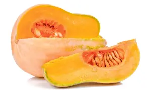 Pomarańczowa dynia, przekrojona na pół, z widocznymi nasionami. Obok leży plasterek tej samej odmiany dyni.