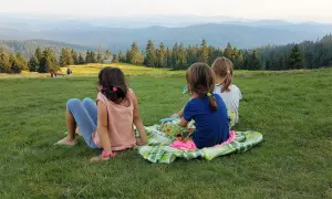 Trzy dziewczynki siedzą na kocu na trawie, podziwiając widok z hali Rysianka.