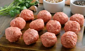 Gotowe do smażenia, obłędne kotlety mielone. Na drewnianej desce leży kilkanaście okrągłych porcji mięsa mielonego, obok pęczek natki pietruszki i czosnek.
