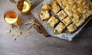 En härlig vegansk morotskaka med glasyr, nötter och citrusskal. Två koppar te med citron står bredvid.