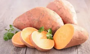 Patates douces entières et tranchées, garnies de persil frais, sur fond de bois. Un délice orangé prêt à être cuisiné.